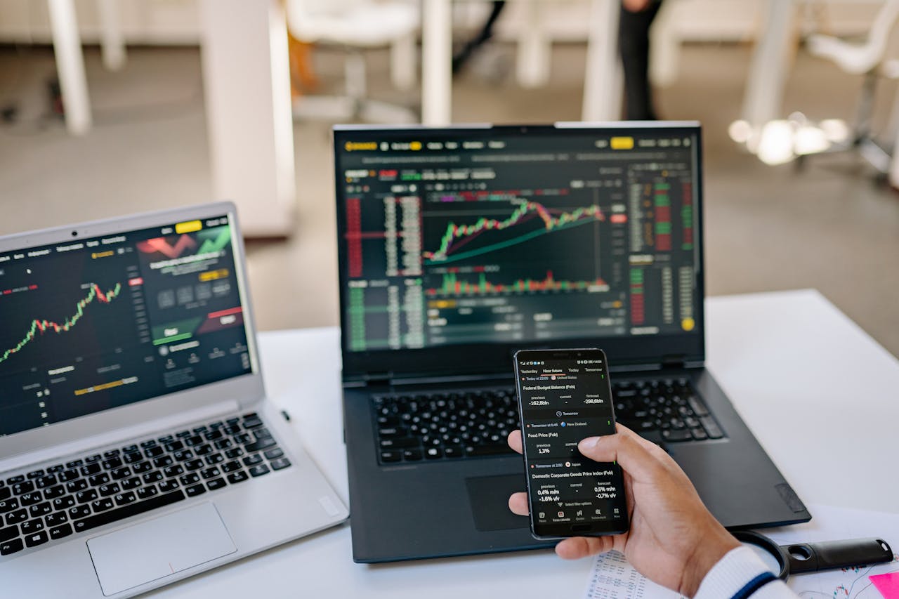 home-hero-bg A professional tracks stock market trends using two laptops and a smartphone, showcasing digital finance tools.
