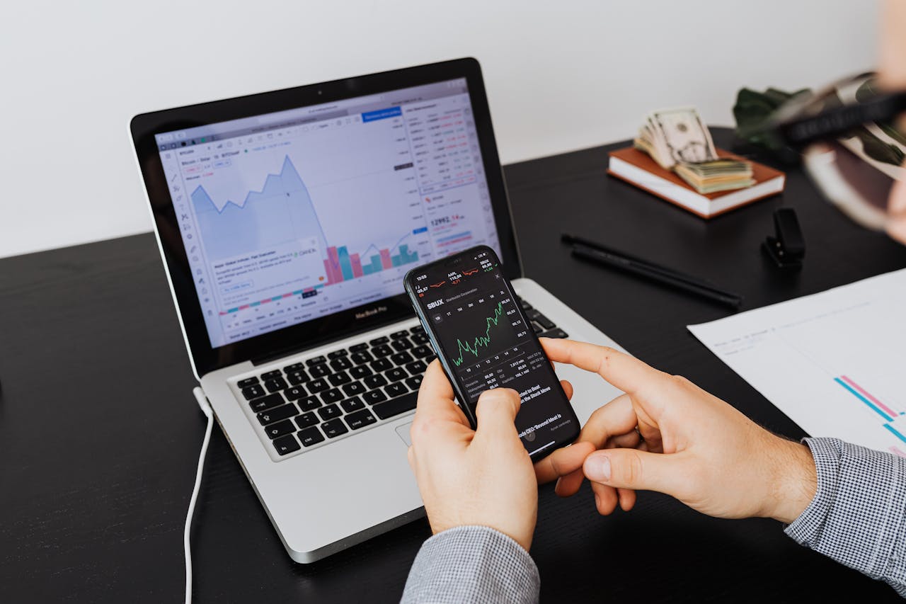 about-01 Person analyzing stock market data on a laptop and smartphone indoors.